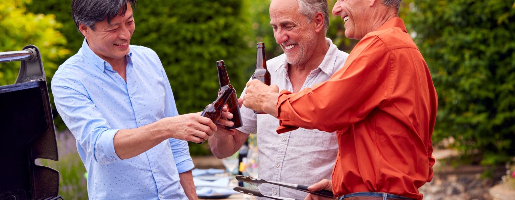 a group of men holding beers cooking on the grill